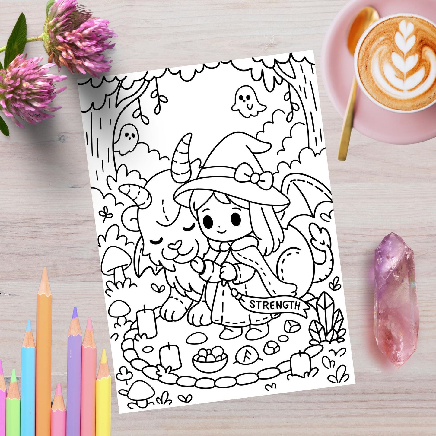 Strength tarot card coloring page from Spooky Forest Tarot Volume 2, featuring a cute witch girl with bow and cape gently holding a smiling goat-like creature with horns in a magical forest circle with candles, mushrooms, crystals, and ghosts. Shown on a wooden surface with colored pencils, pink flowers, a latte, and an amethyst crystal.